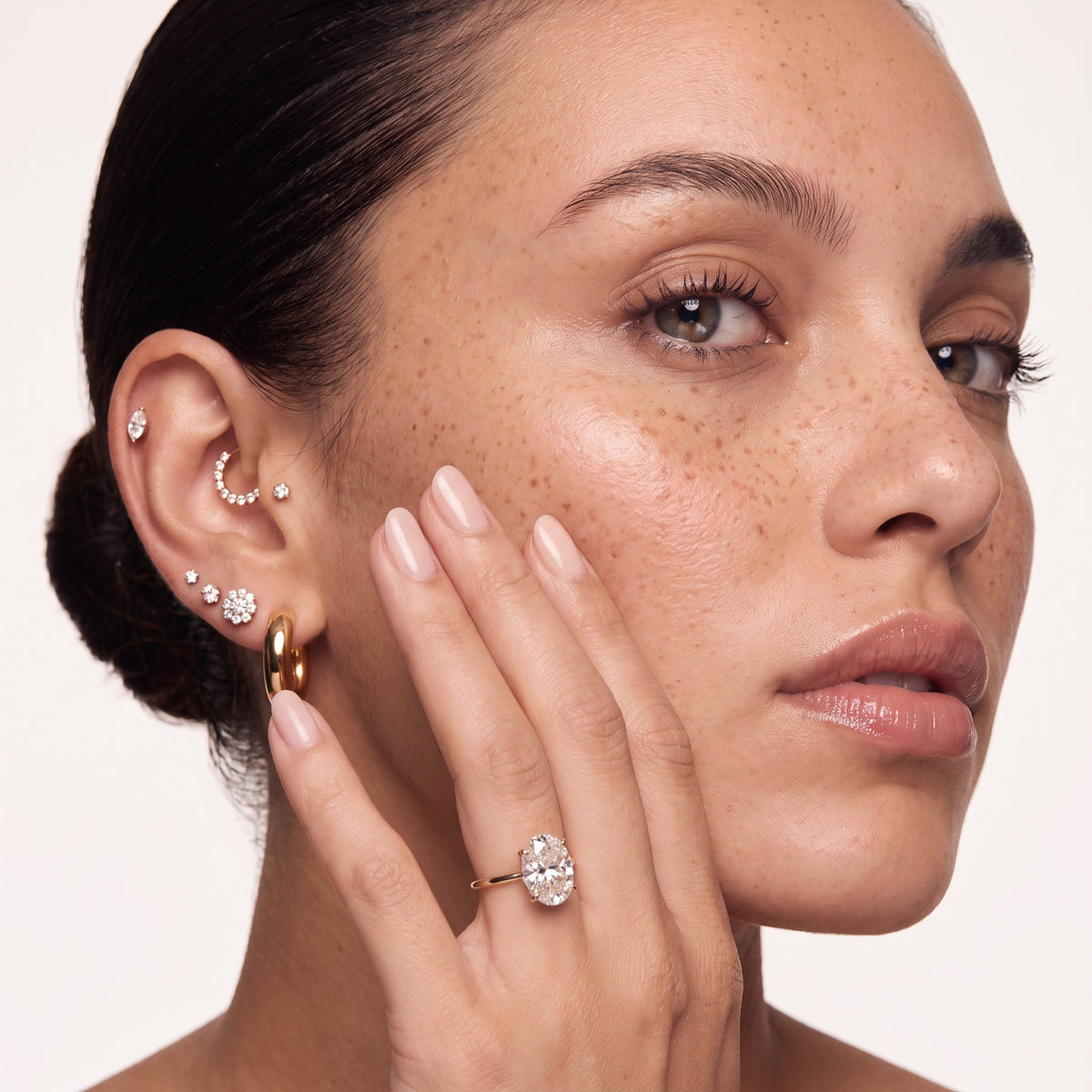 Model wearing a diamond ear stack and oval engagement ring