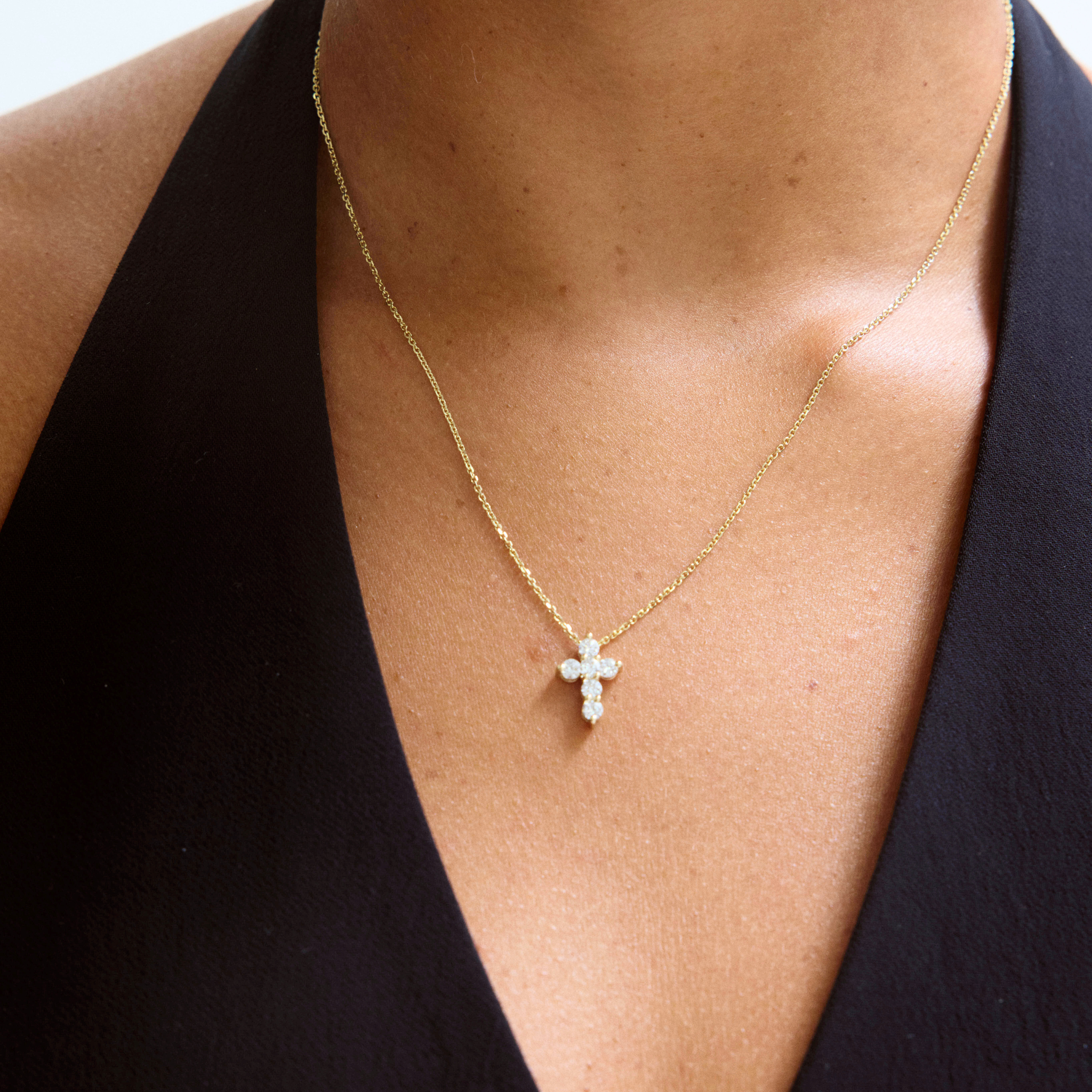 Gold necklace with a cross pendant on a person wearing a black top.